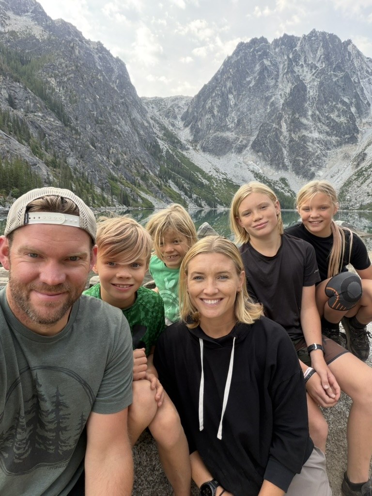 Trae, Christi, and their four children together during a mountain hike by an alpine lake